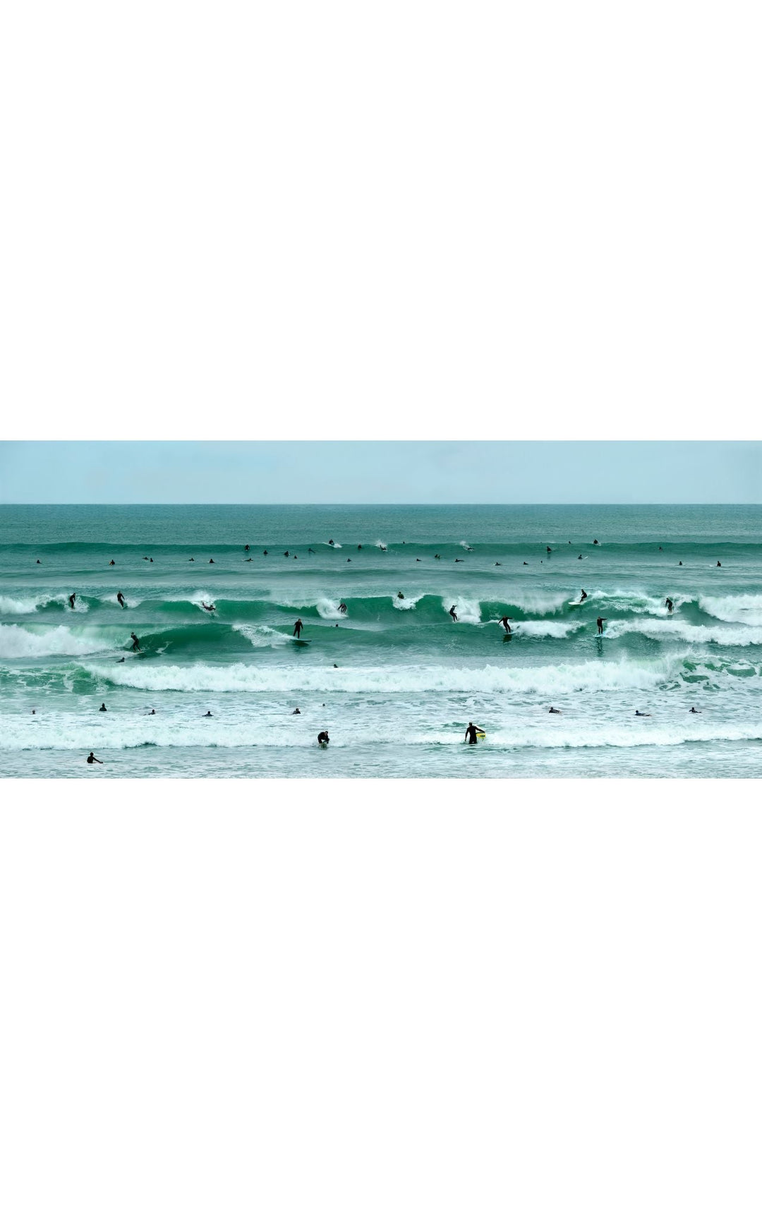 Coastal photography with emerald waves and surfers dotting the shore line of the Pacific Ocean.