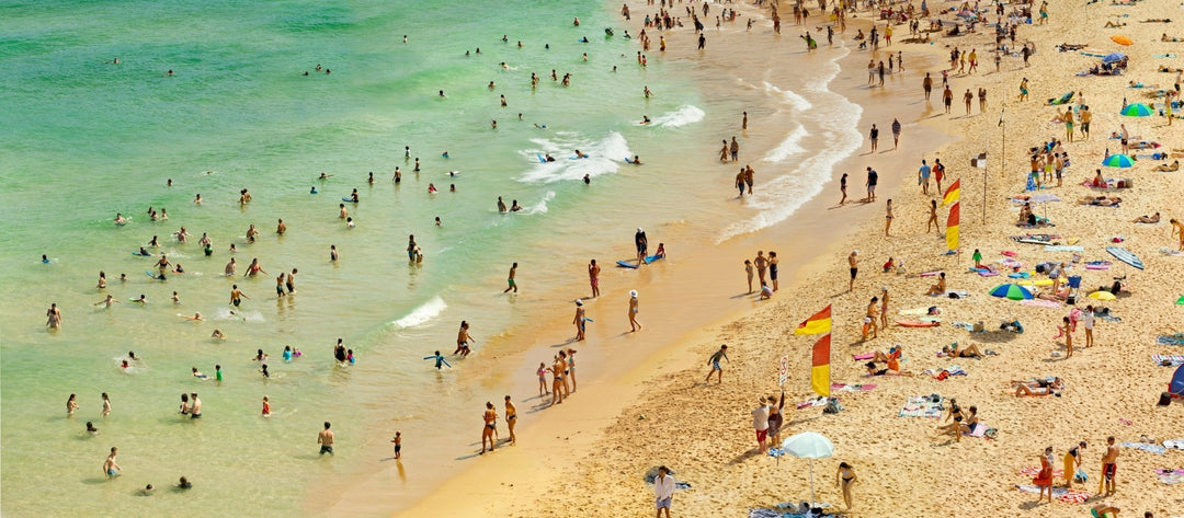 Pacific Ocean beach scene. Beachgoers along emerald clear shoreline.