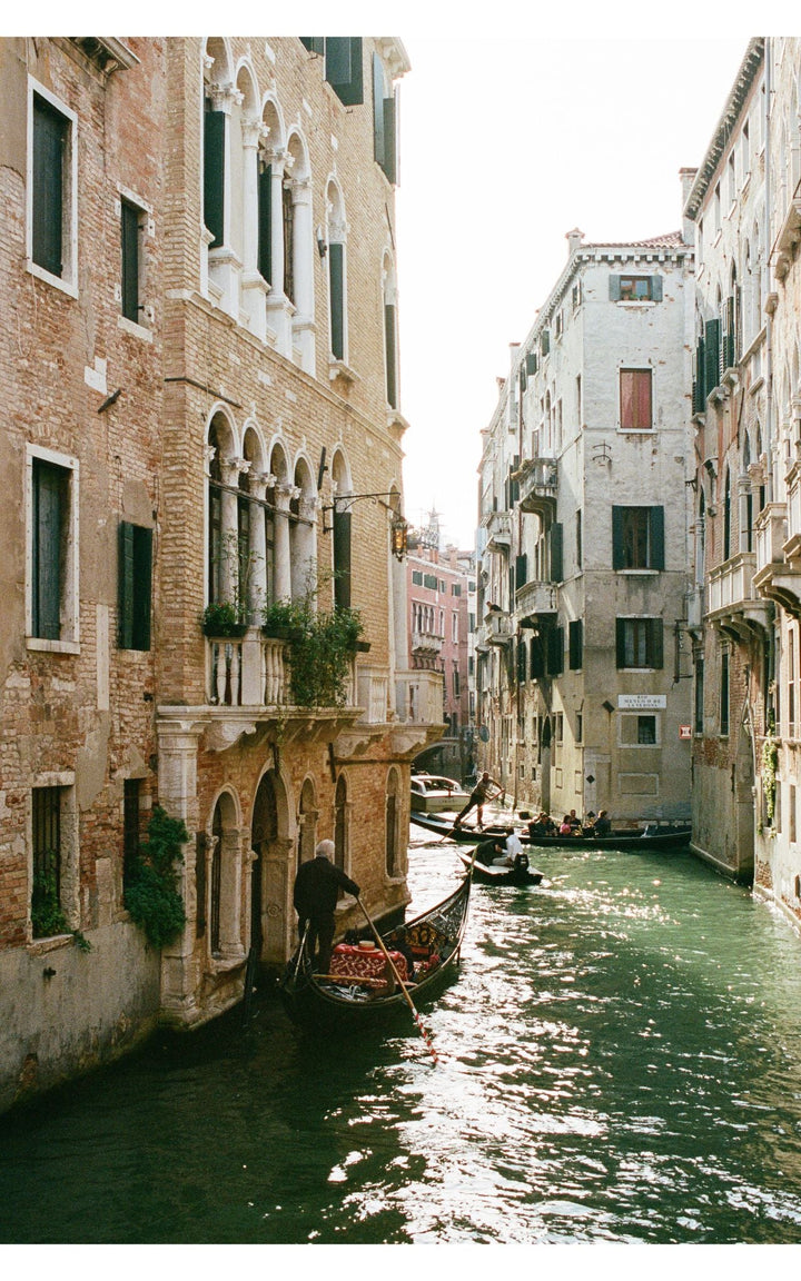 Photograph of a sunlit canal lined with architecture and gondolas.