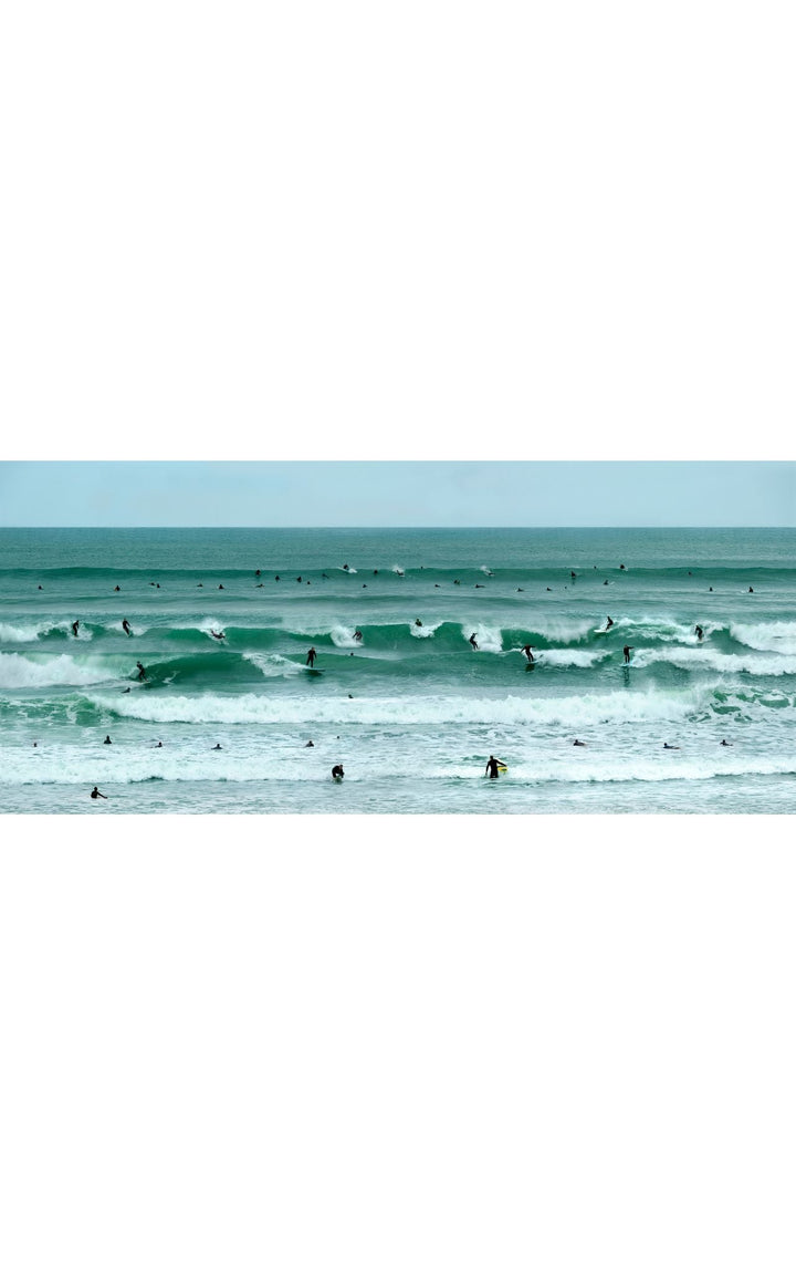 Coastal photography with emerald waves and surfers dotting the shore line of the Pacific Ocean.