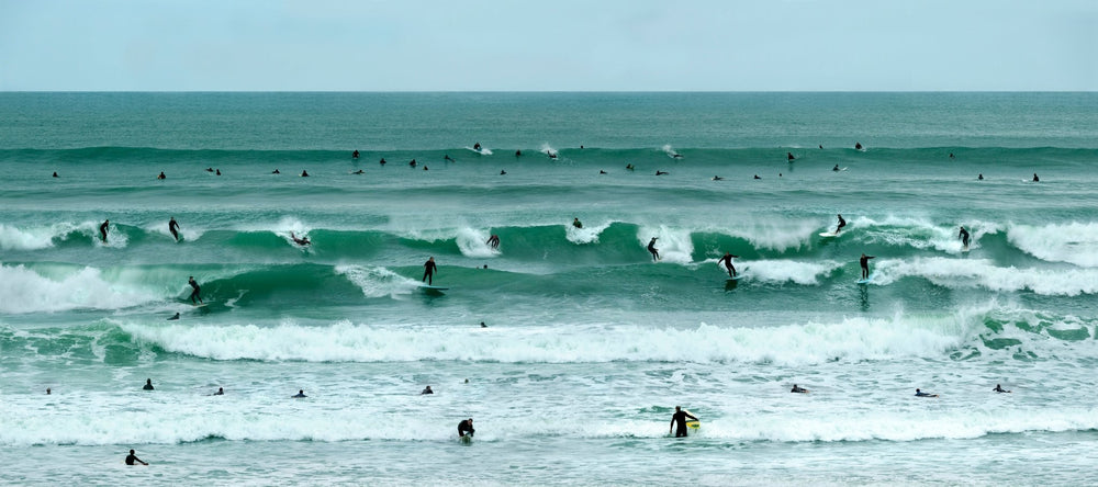 Coastal photography with emerald waves and surfers dotting the shore line of the Pacific Ocean.