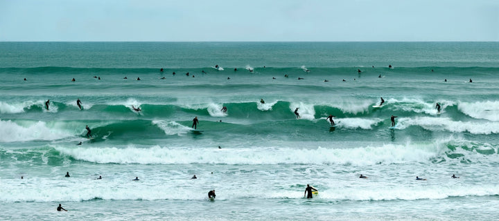 Coastal photography with emerald waves and surfers dotting the shore line of the Pacific Ocean.