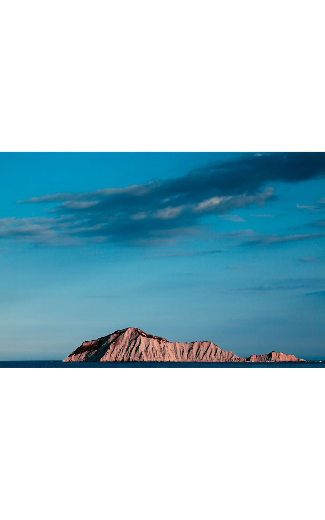 Motu-o-kura island against still waters and dominant blue sky.