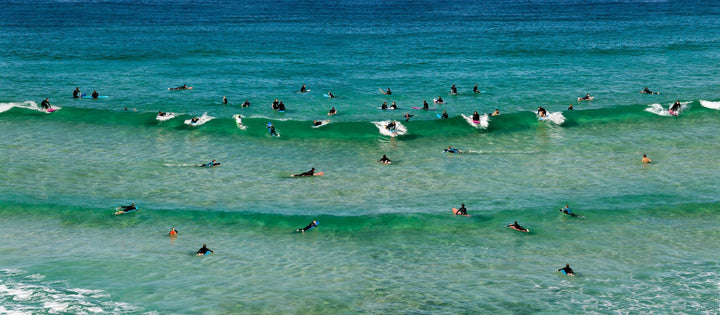 Surfers along rolling waves in crystal clear emerald waters of the Pacific Ocean.