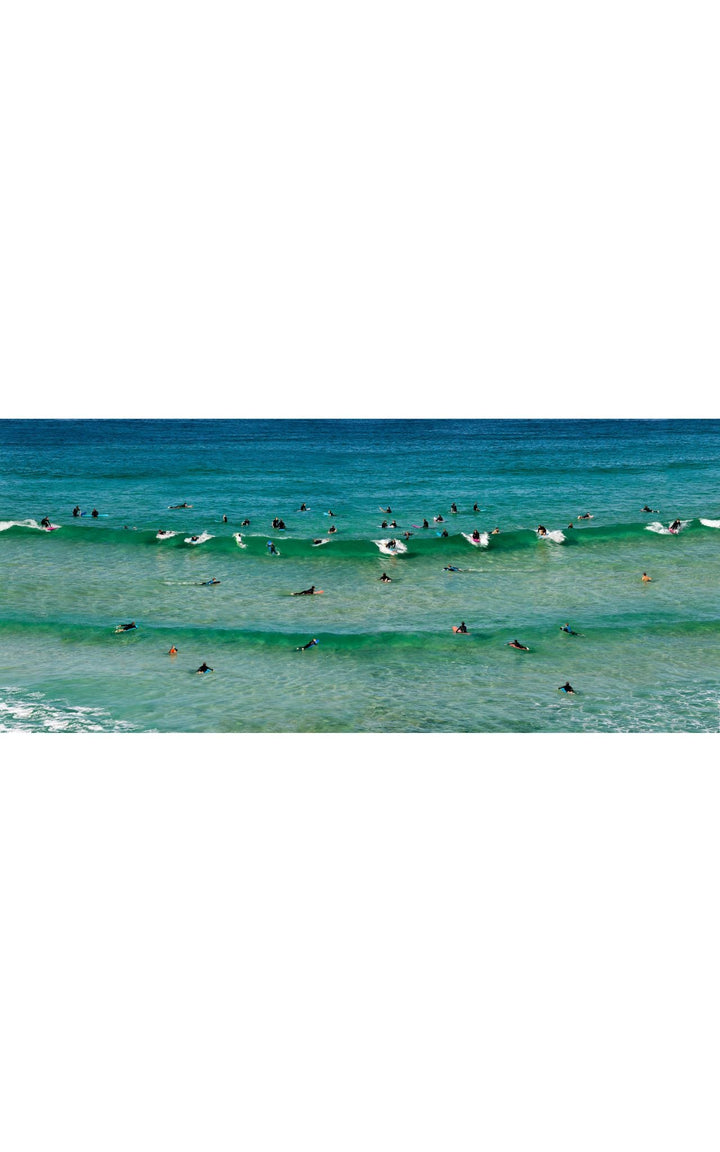 Surfers along rolling waves in crystal clear emerald waters of the Pacific Ocean.