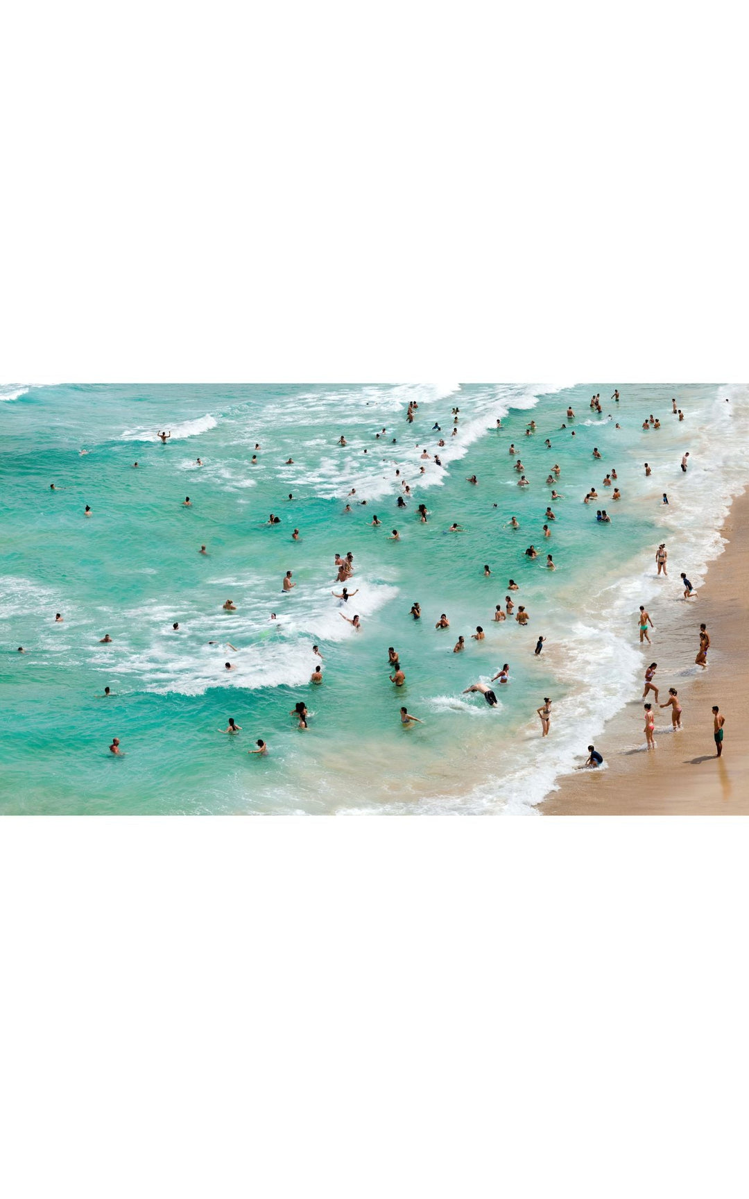 Aerial view of crystal clear emerald ocean with bathers lining the shore.