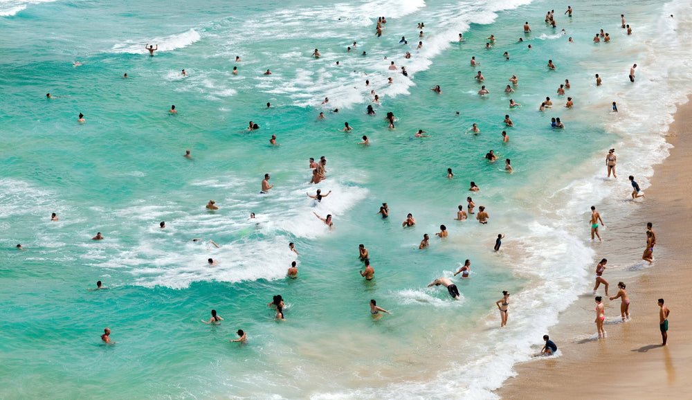 Aerial view of crystal clear emerald ocean with bathers lining the shore.