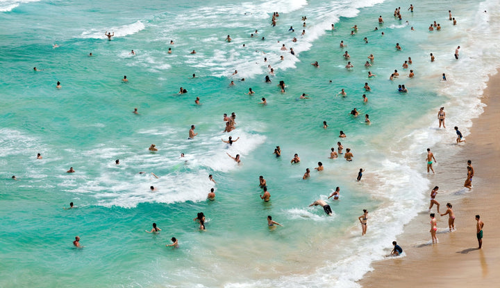 Aerial view of crystal clear emerald ocean with bathers lining the shore.