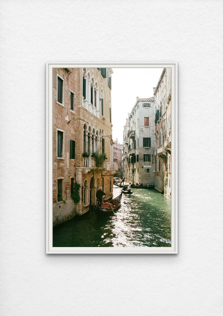 Photograph of a sunlit canal lined with architecture and gondolas.