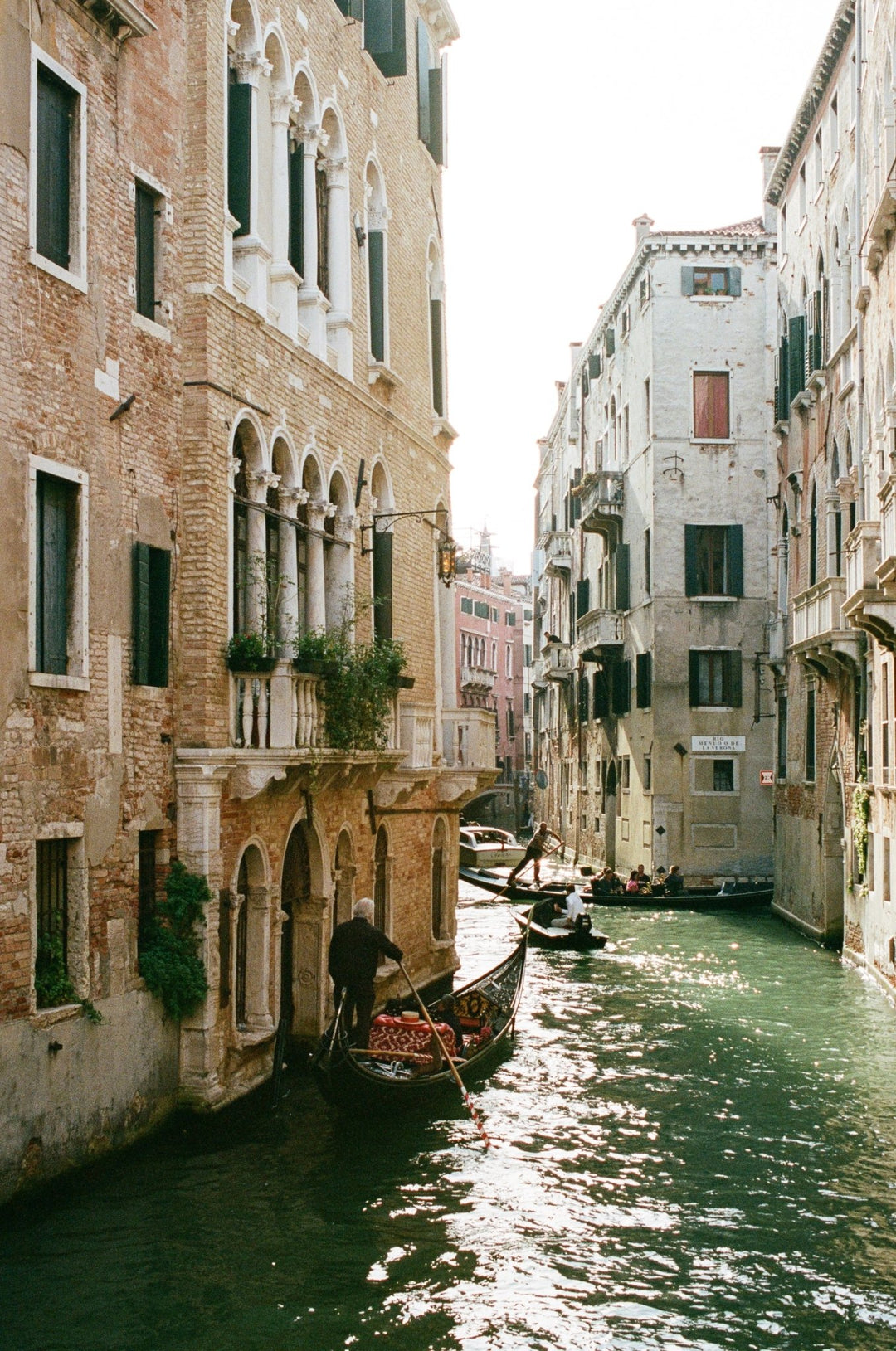 Photograph of a sunlit canal lined with architecture and gondolas.