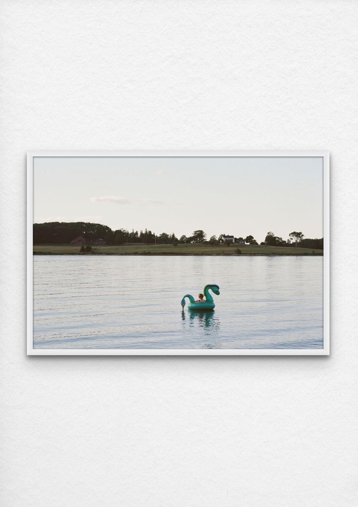 Photograph of woman floating on lake near a lake house in Maine framed in white and installed - Artly International